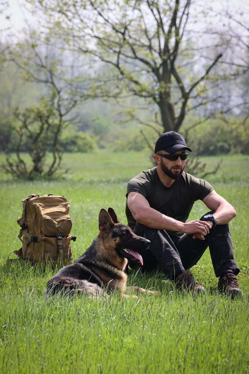 man in cap sitting with german shepherd on grass